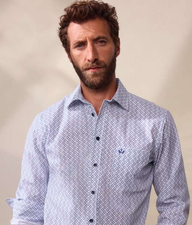 Ein Mann trägt ein helles, gemustertes Hemd mit dunkler Hose. Dazu kombiniert er eine dunkelblaue Weste für einen eleganten, klassischen Look.