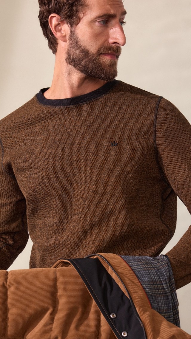 Ein Mann trägt einen braunen Pullover, kombiniert mit einer passenden wattierten Cordjacke. Der Look wirkt herbstlich, lässig und trotzdem stilvoll.