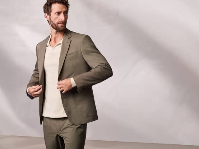 Ein Mann trägt ein Anzug aus Baumwollmix in Khaki, darunter einen gerippten Polopullover in Natur.