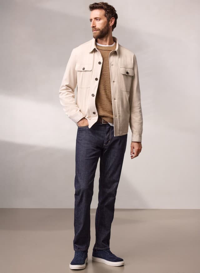 Ein Mann trägt eine Hemdjacke aus Microvelours in Beige, darunter einen Pullover in der Farbe Latte und dazu eine Jeans.