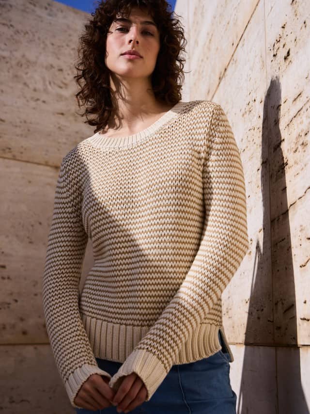 Eine Frau steht vor einer Natursteinwand und trägt einen Pullover mit dezentem Streifen in Creme, dazu eine Marlene Jeans. Eine Frau steht vor einer Natursteinwand und trägt einen Pullover mit dezentem Streifen in Creme, dazu eine Marlene Jeans.