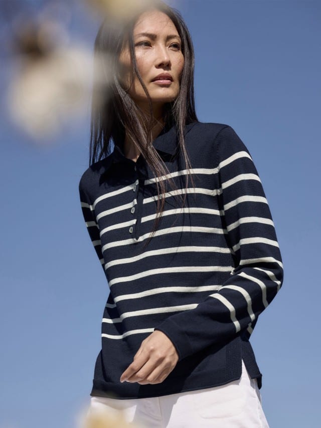 Eine Frau steht im Freien vor blauem Himmel und trägt einen dunkelblauen Pullover mit weißen Streifen zu einer hellen Hose. Eine Frau steht im Freien vor blauem Himmel und trägt einen dunkelblauen Pullover mit weißen Streifen zu einer hellen Hose.