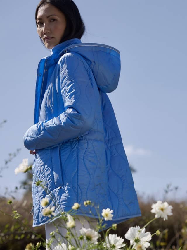 Eine Frau steht im Freien und trägt eine hellblaue gesteppte Jacke mit Kapuze. Eine Frau steht im Freien und trägt eine hellblaue gesteppte Jacke mit Kapuze.