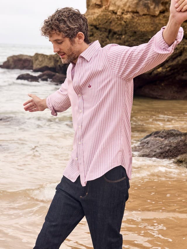 Ein Mann an der Küste trägt ein rot gestreiftes Hemd, dazu eine Charakter-Jeans.
