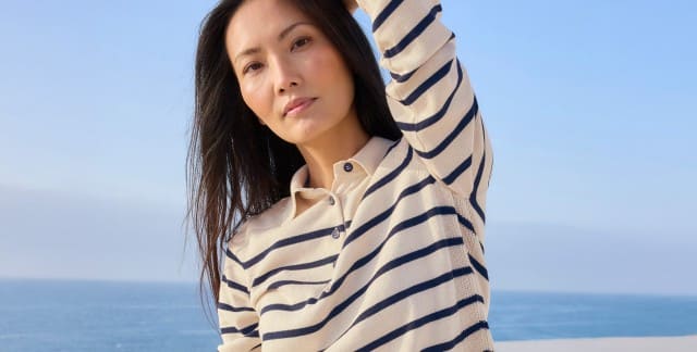 Ein Frau steht am Meer und trägt einen gestreiften Polo-Pullover.
