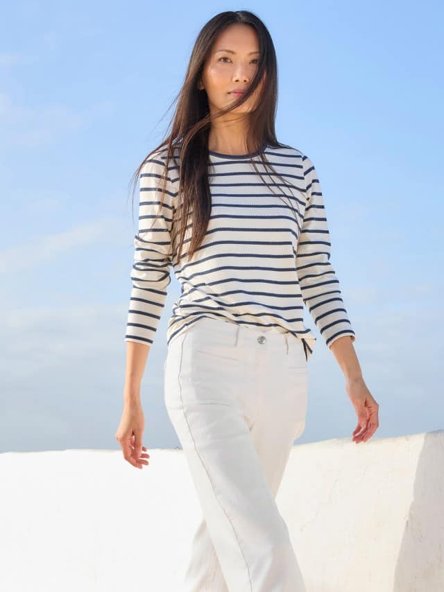 Eine Frau trägt ein weiß‑blau gestreiftes Langarmshirt zu einer weißen Hose, was frisch, maritim und entspannt wirkt.