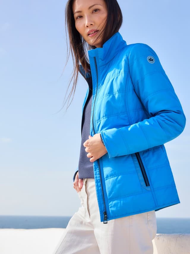 Eine Frau trägt eine leuchtend blaue Steppjacke zu dunkelblauem Shirt und heller Hose, was frisch, sportlich und unkompliziert wirkt.