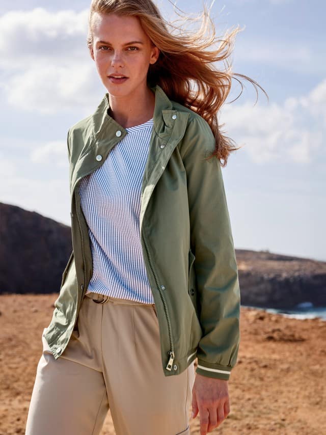 Eine Frau trägt eine Blousonjacke in Khaki, darunter ein Streifenshirt in Meerblau und dazu eine helle Cargohose.