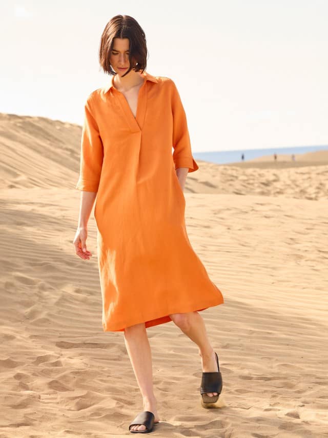 Eine Frau steht in den Dünen und trägt ein Leinenmixkleid in Dunkelorange.