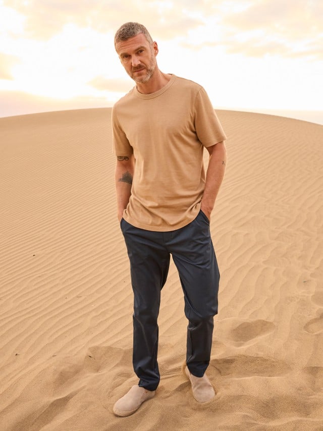Ein Mann steht in den Dünen und trägt ein helles Shirt, dazu eine Chino in Marine. Ein Mann steht in den Dünen und trägt ein helles Shirt, dazu eine Chino in Marine.