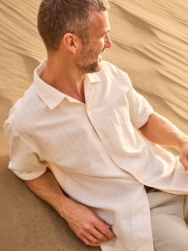 Ein Mann liegt entspannt im Sand einer Düne und trägt ein helles Kurzarmhemd. Ein Mann liegt entspannt im Sand einer Düne und trägt ein helles Kurzarmhemd.