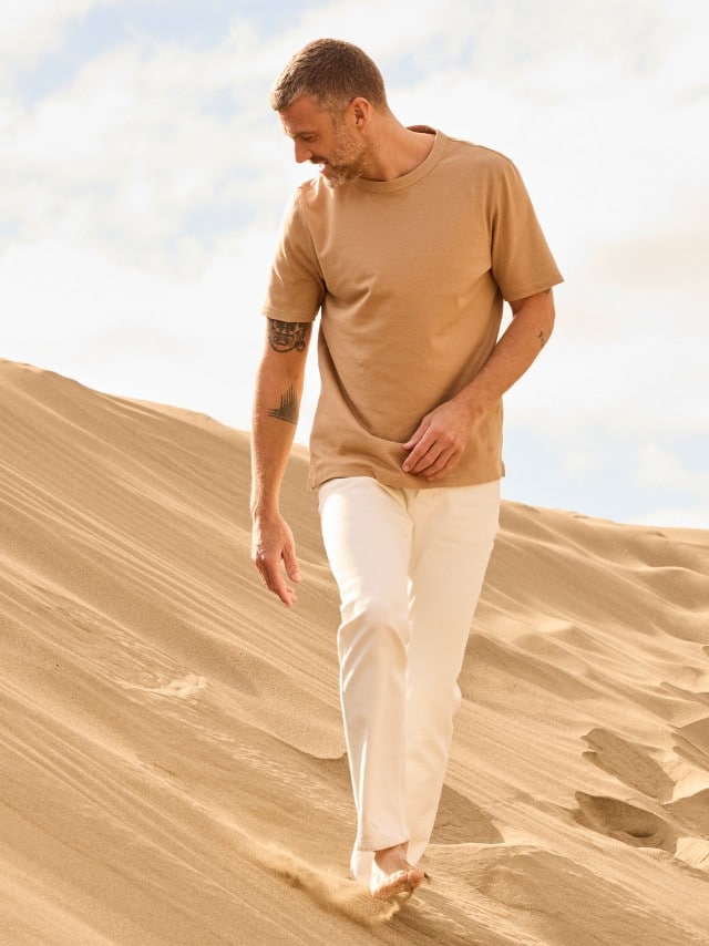 Ein Mann in den Dünen, trägt ein helles Leinen Shirt und dazu eine weiße Hose. Ein Mann in den Dünen, trägt ein helles Leinen Shirt und dazu eine weiße Hose.