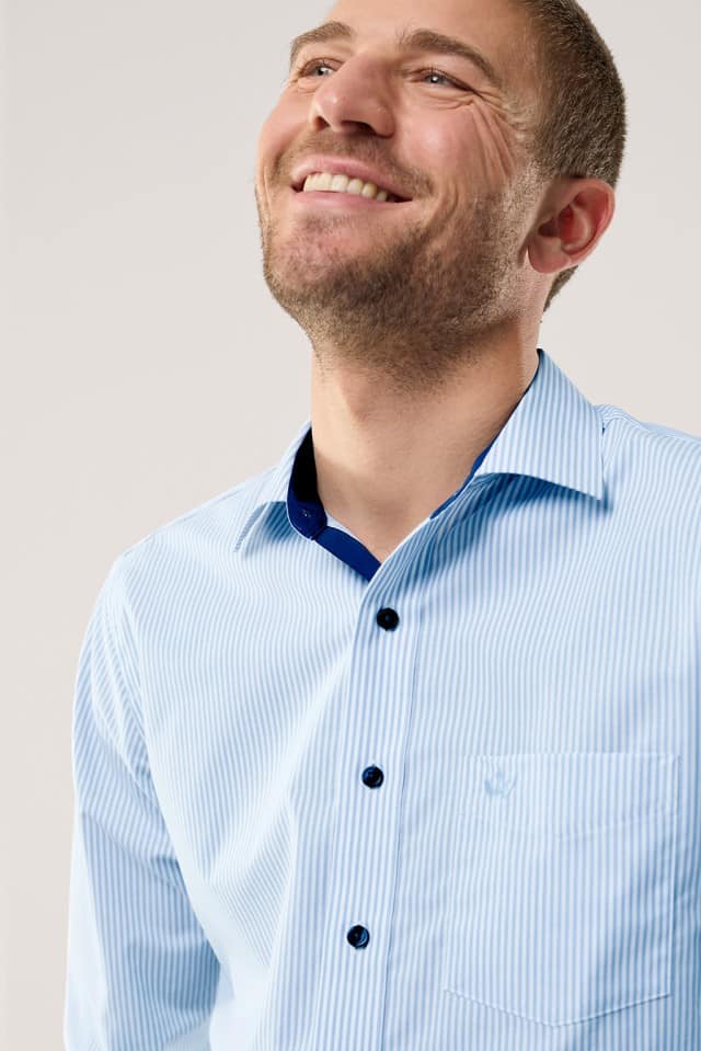 Ein Mann trägt ein hellblau‑weiß gestreiftes Hemd und lächelt nach oben.