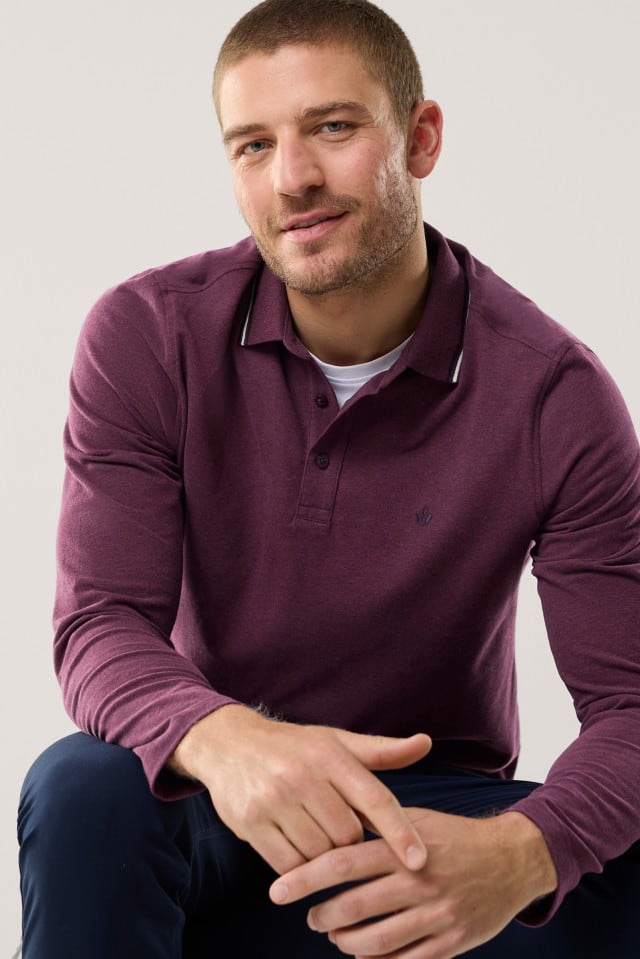 Ein Mann mit kurzem Haar und Bart trägt ein langärmliges, weinrotes Poloshirt mit dezentem Logo auf der Brust und einem Kragen mit feiner heller Zierlinie, unter dem ein weißes T-Shirt hervorschaut.