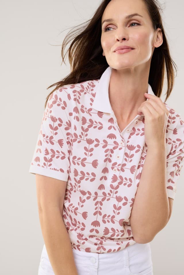 Eine Frau trägt ein Poloshirt Frischekick in der Farbe Tulpenspiel Rosenholz, dazu eine weiße Hose.