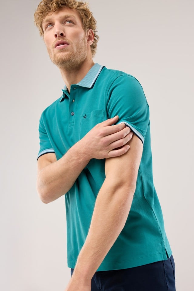 Ein Mann trägt ein Pique-Polo Hitzefrei in Uni Aqua dazu eine dunkle Hose.