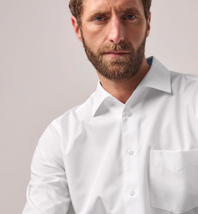Bärtiger Mann in weißem Hemd mit Brusttasche vor hellem Hintergrund.