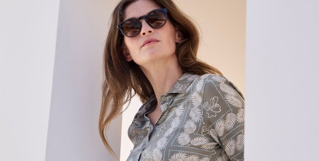 Eine Frau mit Sonnenbrille, die eine grau-grüne Bluse mit weißem floralem Muster trägt.