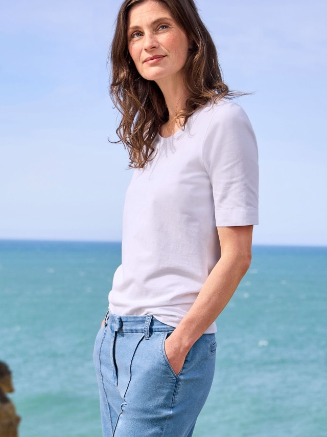 Eine Frau trägt ein schlichtes, weißes T-Shirt und eine hellblaue Hose. Das Outfit wirkt minimalistisch und sommerlich.