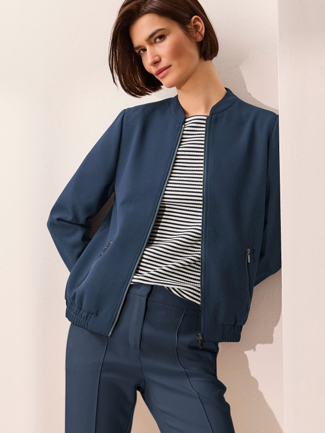 Eine Frau trägt einen Kofferblouson in Marine, darunter ein gestreiftes Shirt und dazu eine Hose in Marine.