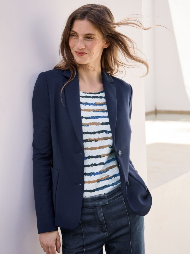 Eine Frau trägt einen Jersey Blazer in Marine, darunter ein gestreiftes Shirt und dazu eine Jeans.