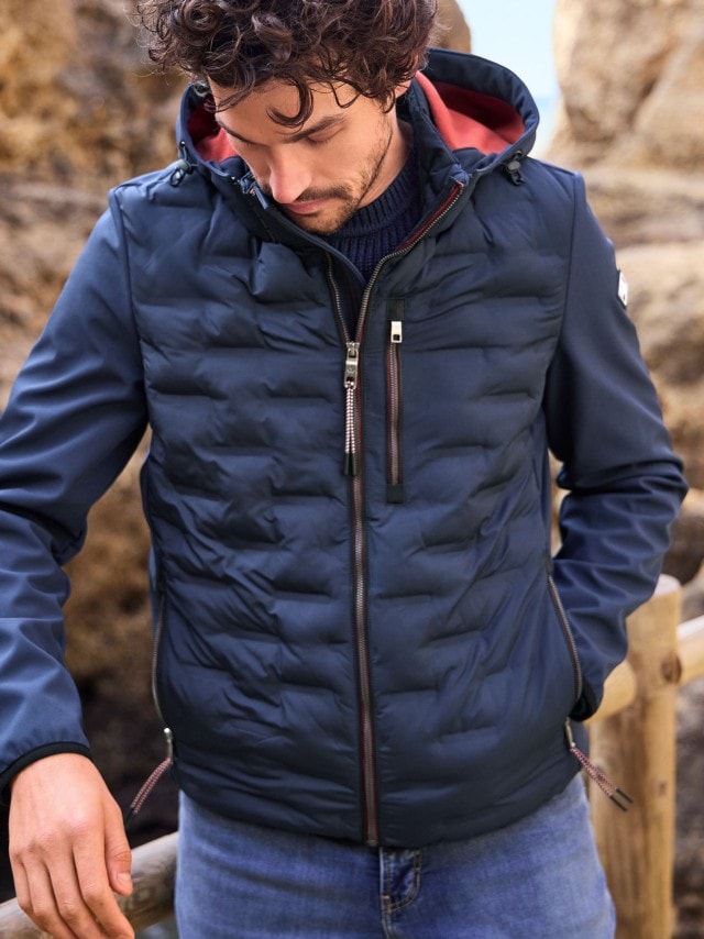 Ein Mann steht vor einem Felsen und trägt den Windlock Klima Blouson in Marine, dazu eine Jeans.