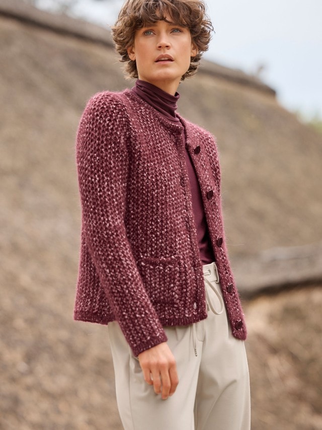 Eine Person trägt eine grob gestrickte, bordeauxrote Strickjacke über einem Rollkragenpullover in passender Farbe. Dazu kombiniert sind helle, weite Hosen für einen eleganten und gemütlichen Look.