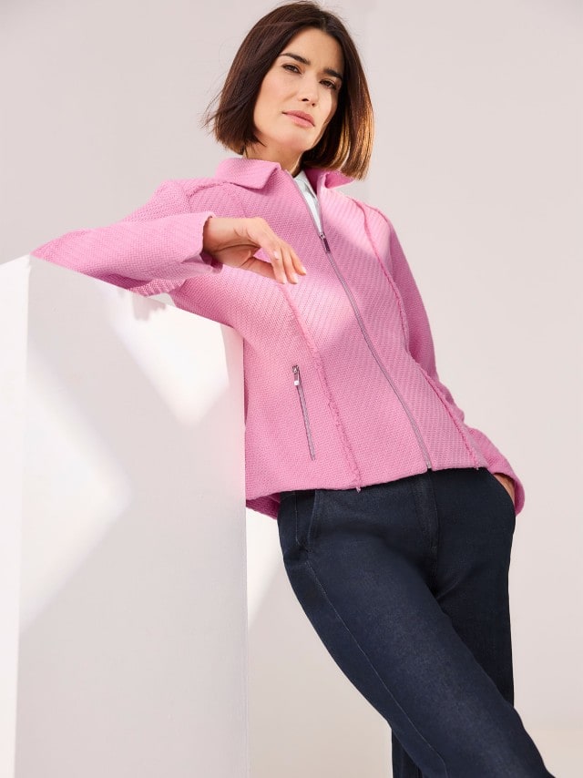 Eine Frau trägt einen Boucleblazer mit Fransenkante in Soft Pink, dazu eine schwarze Hose.