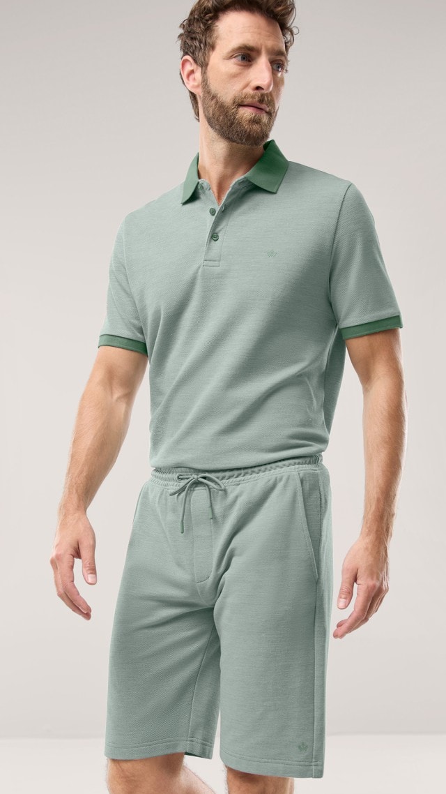 Ein Mann trägt ein Freizeitpolo Extraglatt in Salbei, dazu die passende Freizeitshorts Extraglatt. Ein Mann trägt ein Freizeitpolo Extraglatt in Salbei, dazu die passende Freizeitshorts Extraglatt.