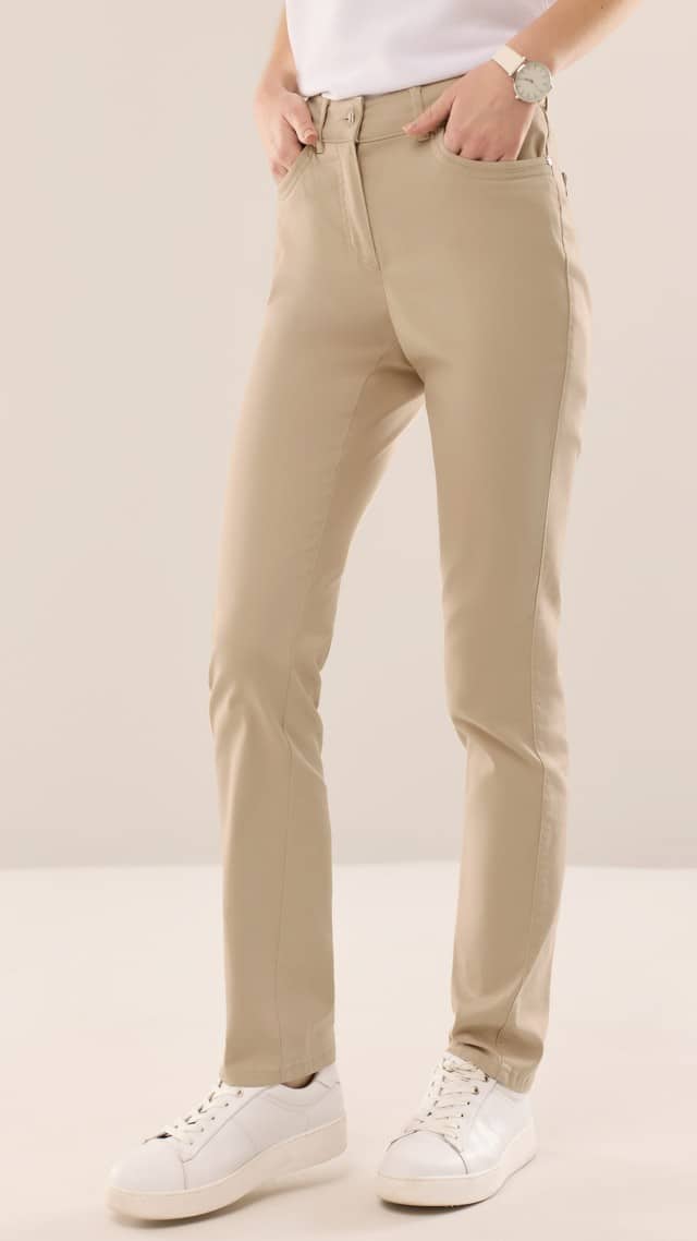 Eine Person trägt eine beige, schmal geschnittene Hose aus glattem Stoff und weiße Sneaker. Der Look ist schlicht, bequem und vielseitig kombinierbar.