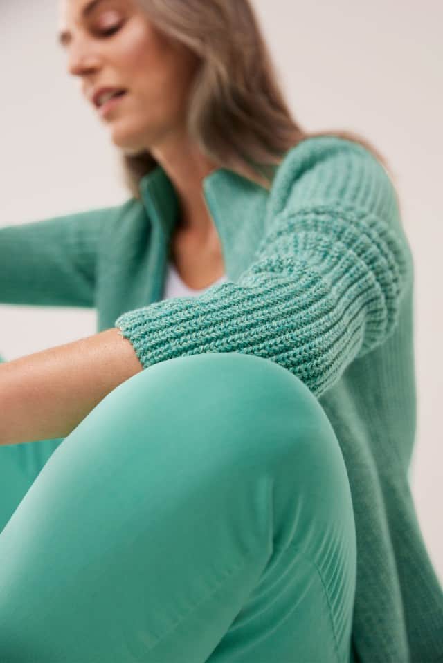 Eine Frau trägt eine Strickjacke in Pfefferminz, dazu die passende Hose und sitzt auf dem Boden.