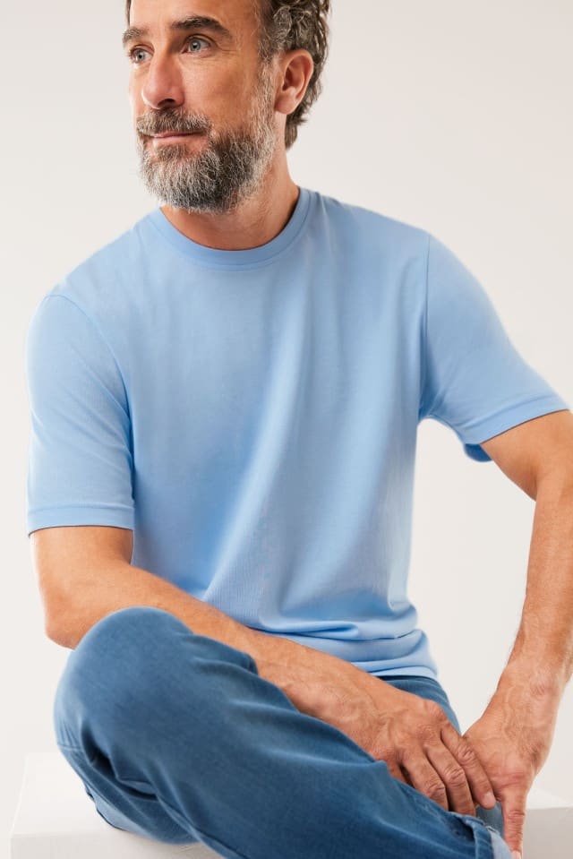 Ein Mann trägt ein T-Shirt mit  Rundhalsausschnitt in Hellblau, dazu eine Jeans.