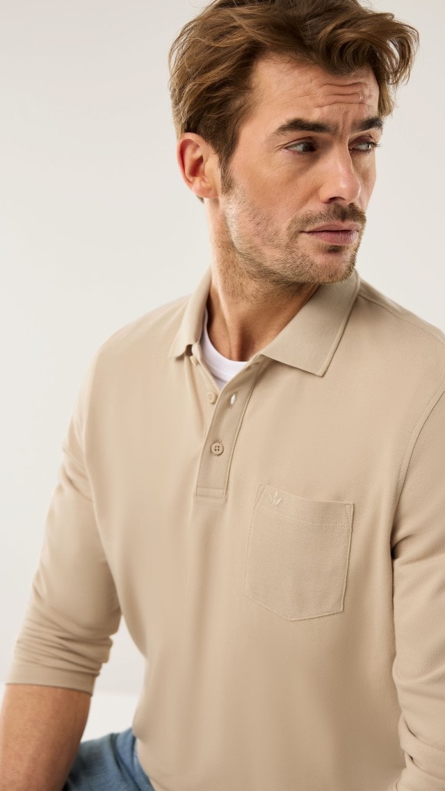 Ein Mann trägt ein Langarm-Poloshirt in Beige, dazu eine Jeans.