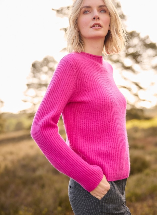 Eine blonde Frau trägt einen Cashmere Pullover in Fuchsia, dazu eine Jeans.