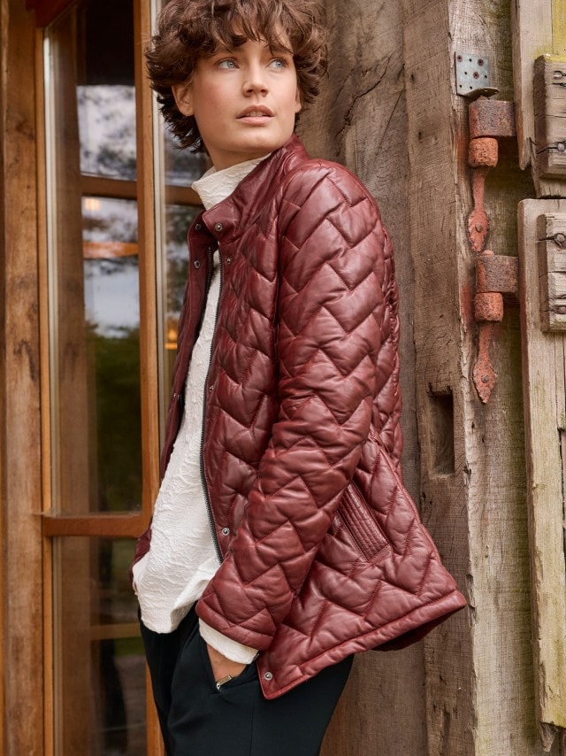 Eine Frau trägt die Lammnappa Jacke Sandwichstepp in der Farbe Chianti, darunter eine weißes Sweatshirt und dazu eine schwarze Hose.