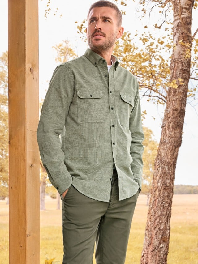 Ein Mann trägt das Soft-Cord Overshirt und hält die Hände in den Taschen einer Hose in Khaki.