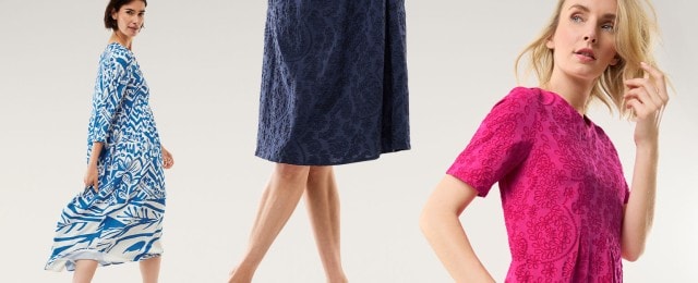 Drei Frauen tragen Kleider: eines mit blau-weißem Muster, eines aus dunkelblauem Stoff mit Struktur und eines in kräftigem Pink mit floralem Muster. Die Kleider wirken sommerlich und elegant.