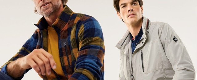 Ein Mann trägt eine gemusterte Fleecejacke in Blau und Braun mit einem senfgelben Shirt, daneben ist eine hellgraue Outdoorjacke zu sehen. Beide Outfits sind modern und lässig.
