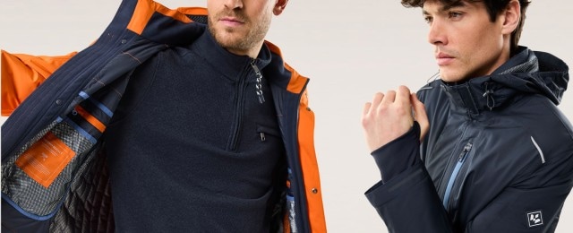 Zwei Männer tragen stylische Outdoor-Jacken: eine in Orange-Blau mit funktionalem Innenfutter, die andere in Marineblau mit Kapuze. Die Kleidung vereint modernes Design und praktische Funktion, ideal für jedes Abenteuer.
