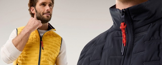 Zwei Männer tragen sportliche Steppwesten: Einer trägt eine gelbe Weste über einem hellen Pullover, der andere eine dunkelblaue Weste mit auffälligem roten Zipper. Die Westen wirken modern und funktional, ideal für einen lässigen Freizeit-Look.