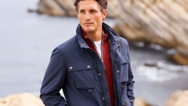 Mann in blauer Jacke steht an einer Felsküste