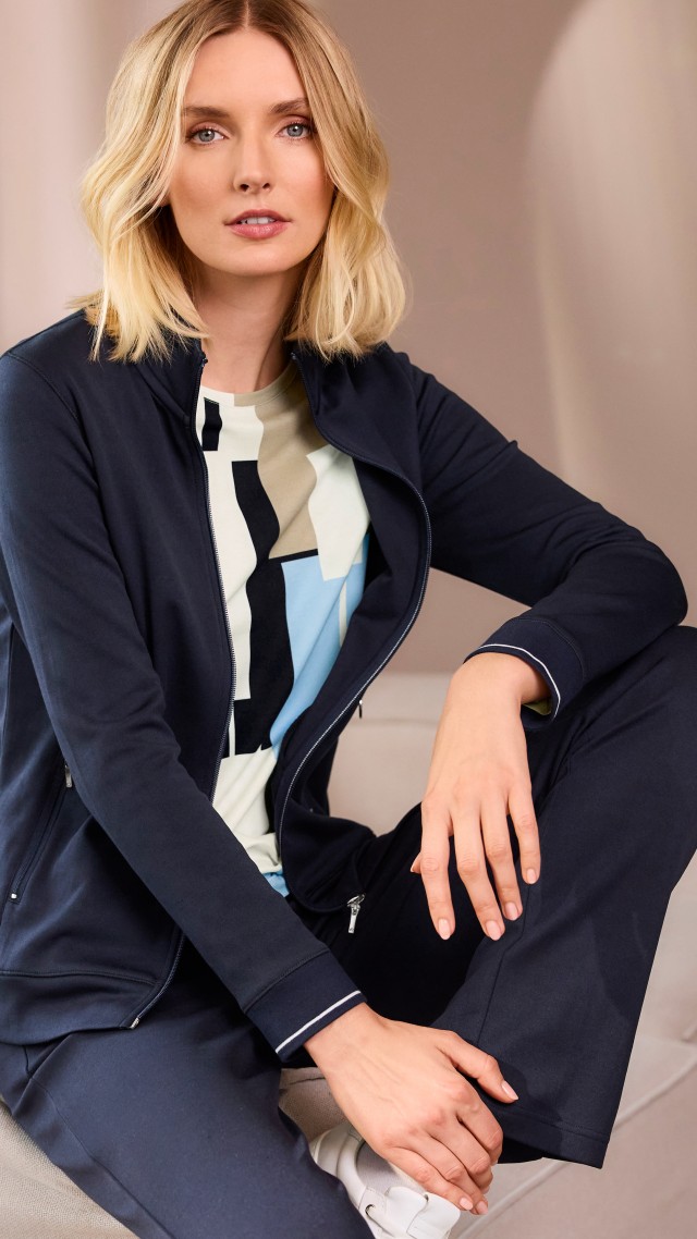 Blonde Frau sitzend in Extraglatt Freizeitjacke in Marine, passender Hose und gemustertem Shirt