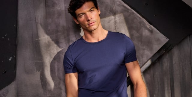 Dunkelhaariger Mann in marineblauem T-Shirt vor dunkler Wand