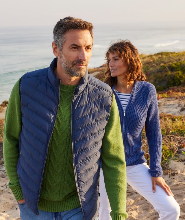 Ein Mann, gekleidet mit einer blauen Weste, und eine Frau mit blauer Strickjacke stehen in einer Düne