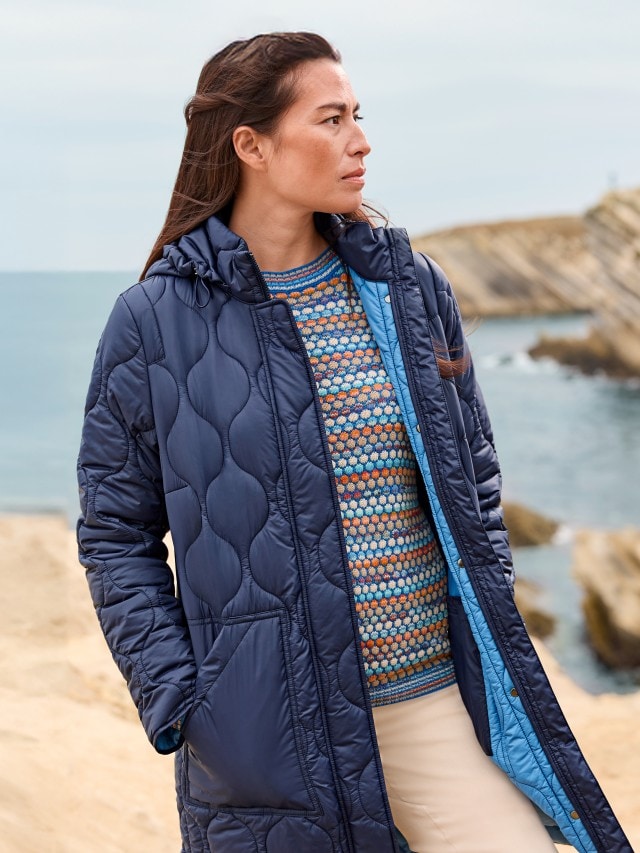 Frau trägt einen blauen Mantel und einen bunten Strickpullover