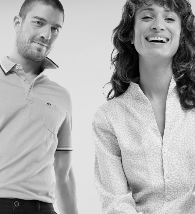 Ein Mann trägt ein kurzärmliges, gemustertes Poloshirt mit Kragen und eine Frau eine langärmlige, gemusterte Bluse; beide wirken fröhlich und entspannt.