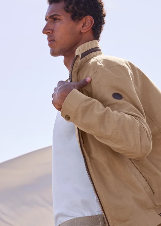 Ein Mann trägt einen Leinenblouson, darunter ein weißes Shirt. Im Hintergrund weht ein großes Leinentuch.