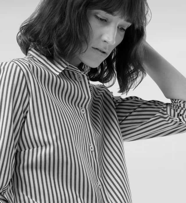 Eine Frau schaut nach unten und trägt eine gestreifte Bluse.