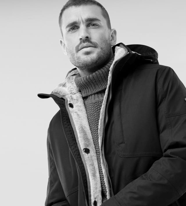 Ein Mann trägt den Aquastop Eisbrecher-Parka, darunter einen Rollkragen-Pullover. Rechts daneben ist eine Frau in einer gestreiften Bluse zu sehen.