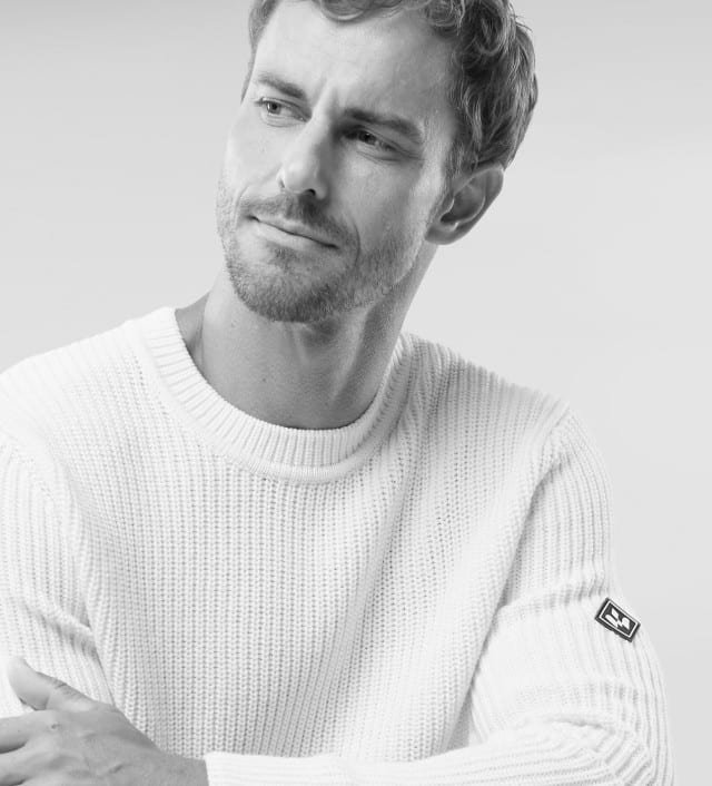 Ein Mann trägt einen grob gestrickten, weißen Pullover mit Rundhalsausschnitt. Sein Stil wirkt schlicht, modern und gemütlich.